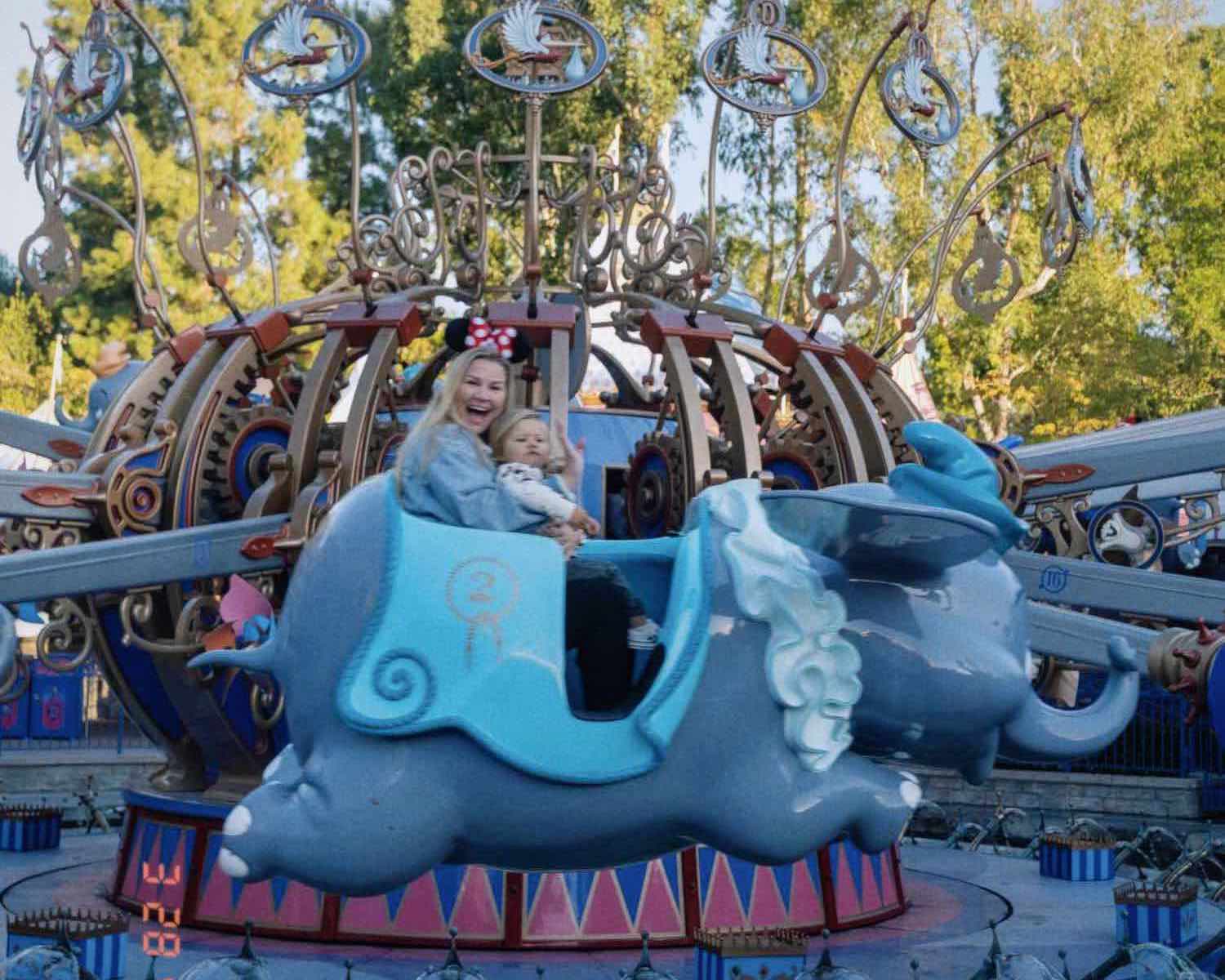 Dumbo ride at Disneyland mid-flight with a slightly blurry blonde woman smiling at camera holding toddler in lap